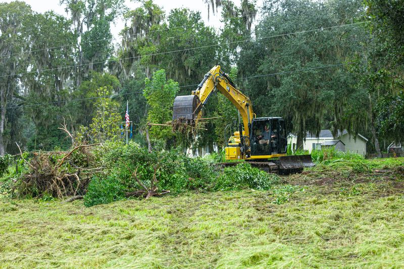 Excavator clearing an overgrown lot with brush piled for haul-off