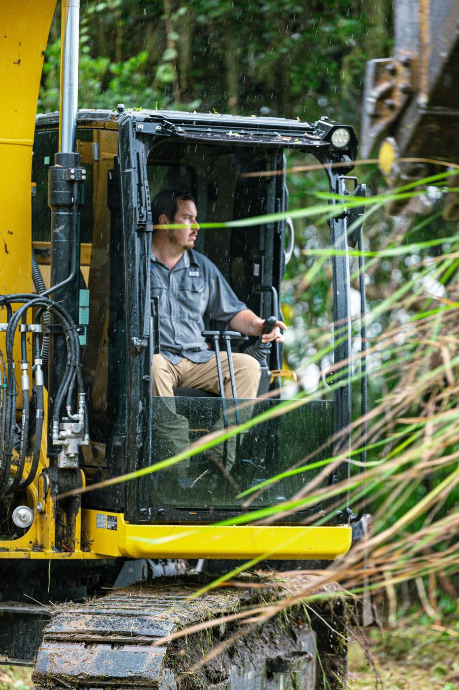 Sam in the excavator cab, side angle, hand on the controls