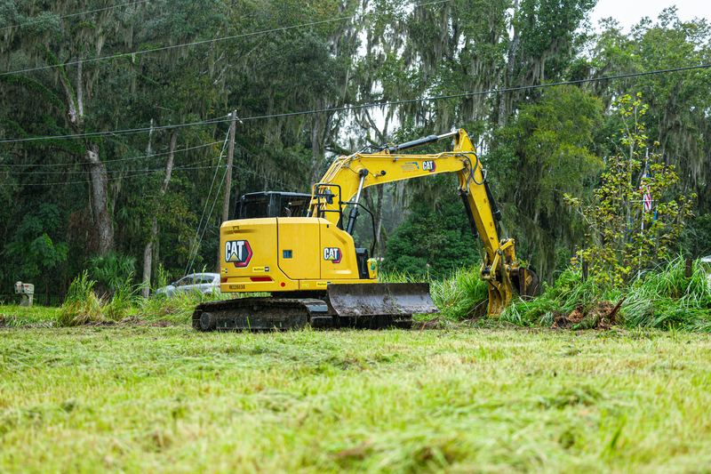 CAT excavator clearing the brush line at the edge of an open field