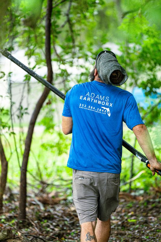 Adams Earthworx crew member walking in with a pole saw